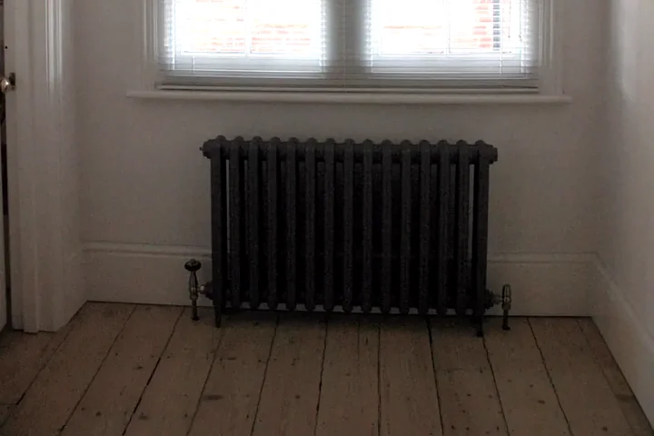 Bare timber floorboards and cast-iron radiator before floor insulation