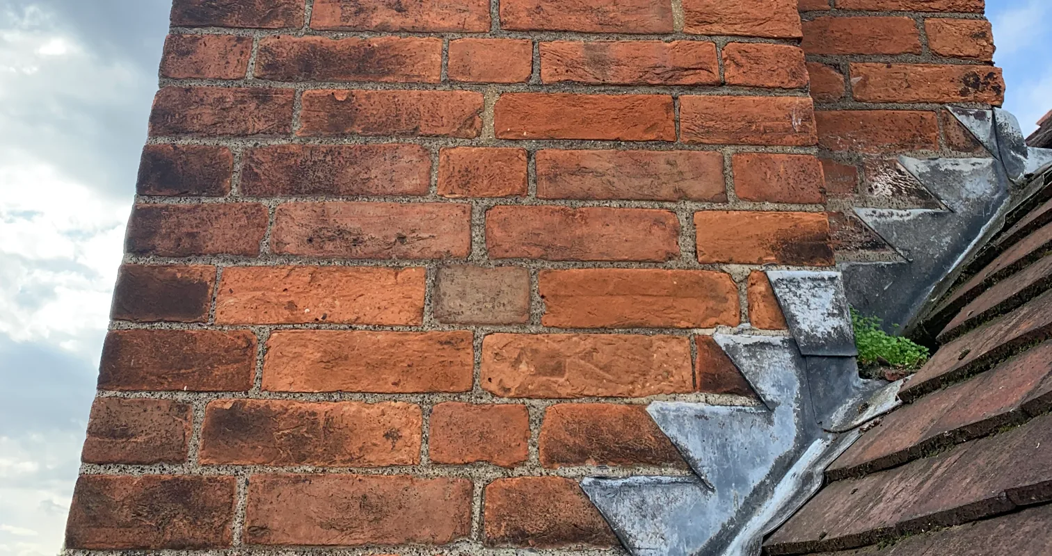 Lime-repointed chimney brickwork with stepped lead flashing over handmade clay tiles