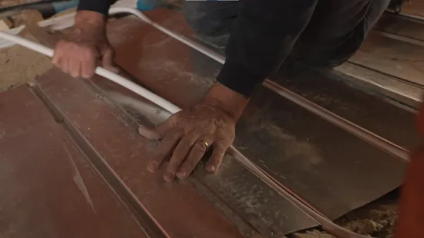 Hands pressing underfloor heating pipe into metal spreader plates over the insulated floor
